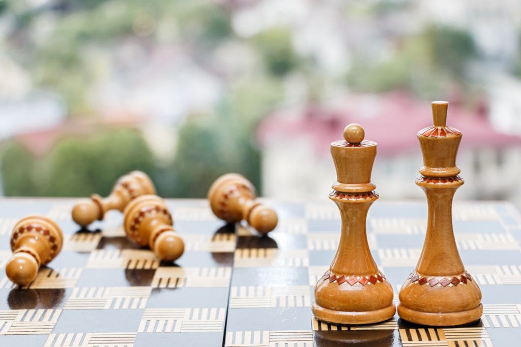 Image of a chess board with king and queen standing amongst fallen pawns