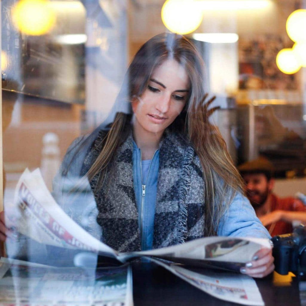 Image taken through a window of a woman reading a newspaper