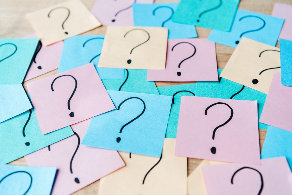 Pastel hued post it notes set on a wooden surface with a question mark inside each note