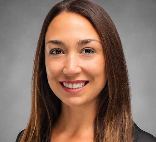Danielle O’Rourke, a woman with long brown hair, smiles at the camera wearing a black crewneck top