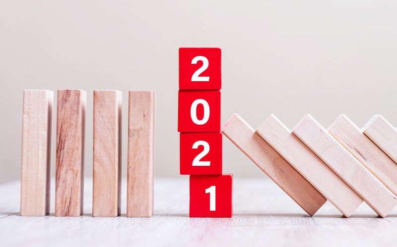 Dominos stacked against bright red blocks that spell out 2021