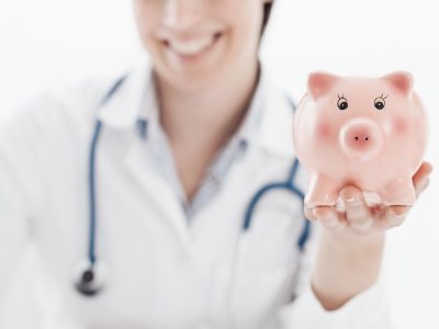 Smiling female doctor holding a piggy bank: health insurance and medical expenses concept