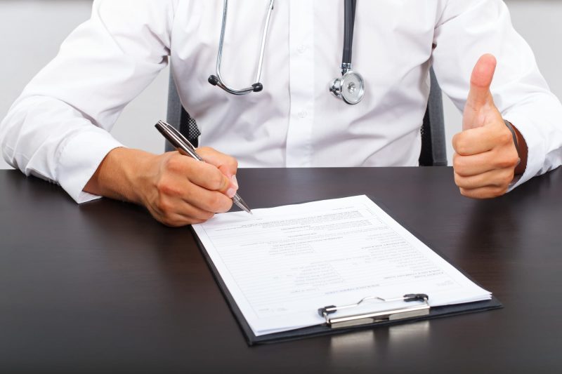 Picture of a doctor hand signing on the medical report and giving a thumbs up